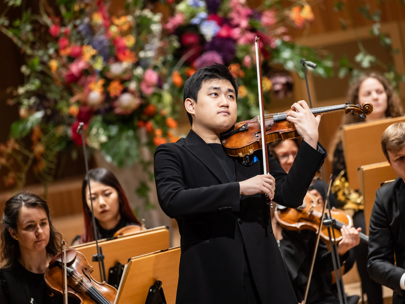 Kyumin Park, Finalist des Joseph Joachim Violinwettbewerb 2024 steht auf der Bühne im Großen Sendesaal des NDr Konzerthauses. Er blickt, die Geige spielend, aufmerksam Richtung Dirigent. Hinter ihm sind die Musiker*innen der NDR Radiophilharmonie zu sehen.
