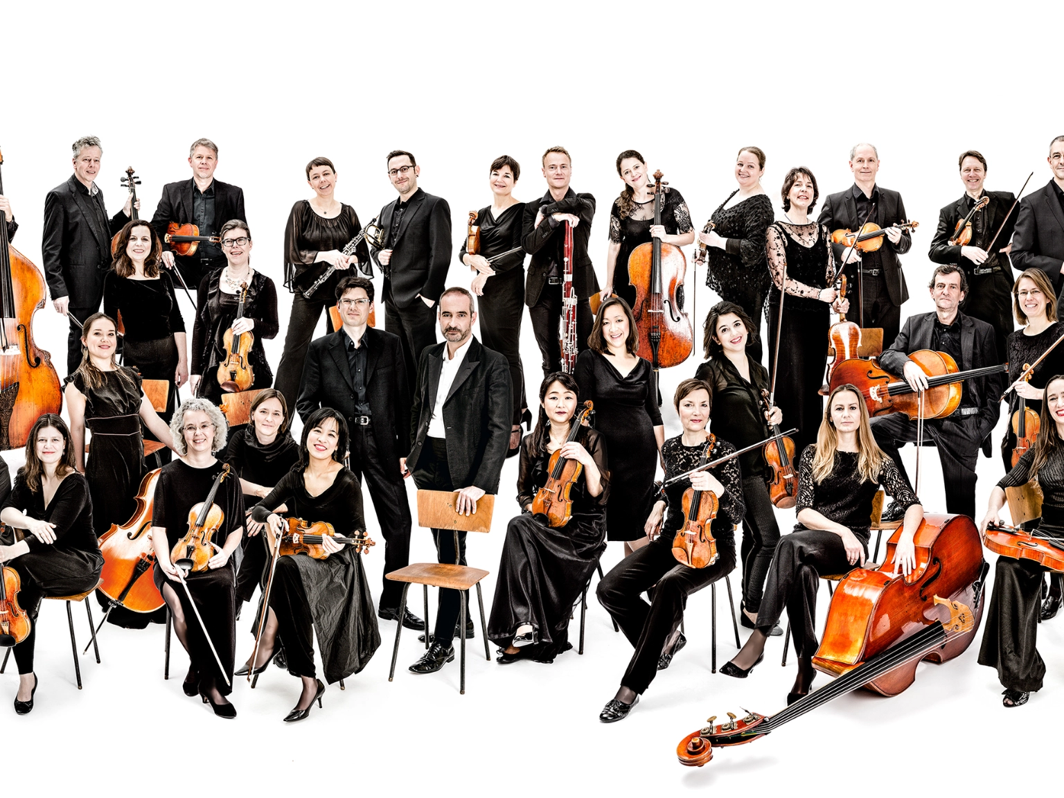 Orchesterbild der Kammerakademie Potsdam. Die Musiker*innen sind mit ihren Instrumenten abgebildet. Der umgebende Raum ist komplett weiß.