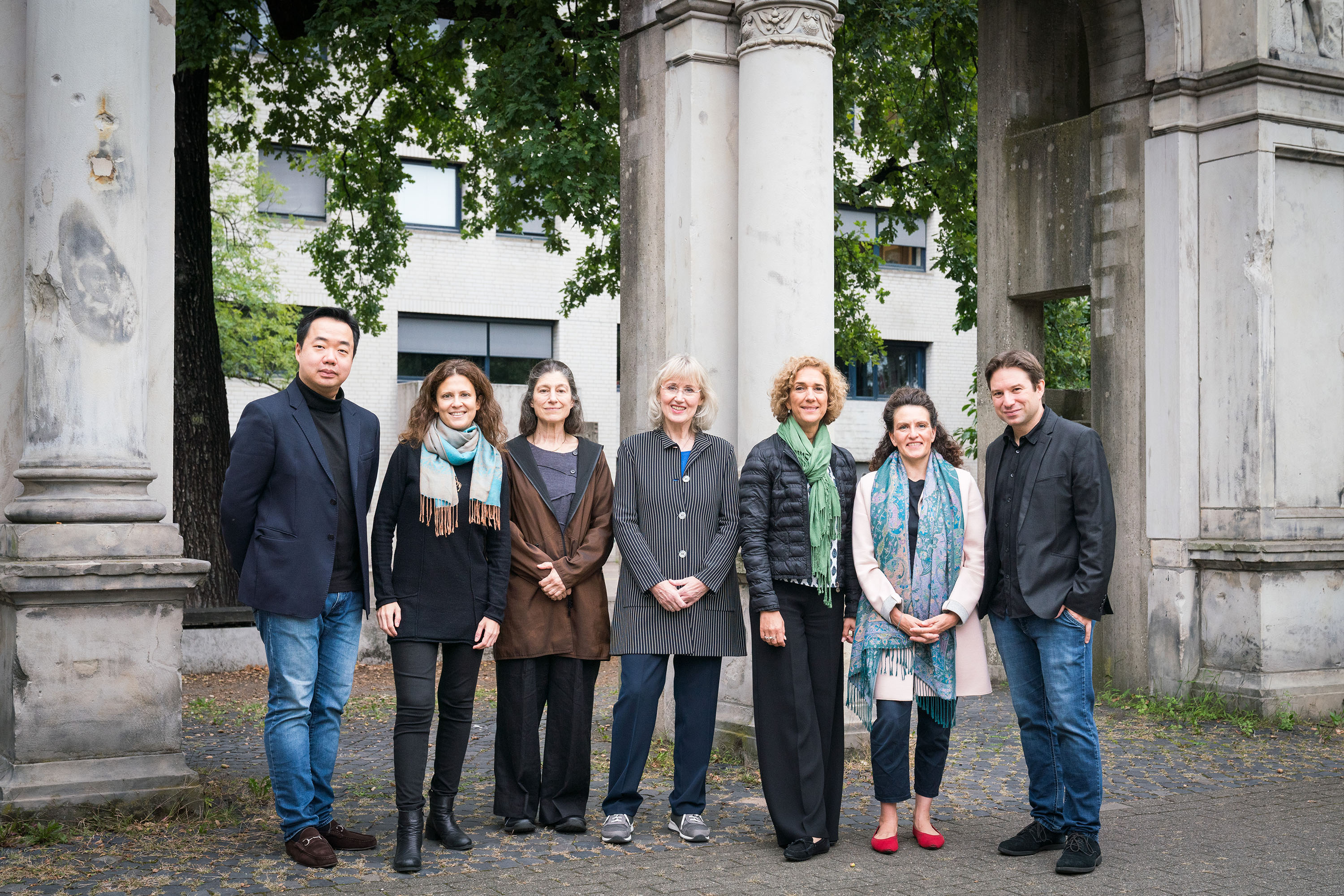 Gruppenbild der Wettbewerbsjury des Joseph Joachim Violinwettbewerbs 2024 (v.l.n.r.: Feng Ning, Liza Ferschtman, Kim Kashkashian, Kathrin Rabus, Juliane Banse, Lorenza Borrani und Stephan Zilias). Sie stehen nebeneinander, draußen vor den Arkaden, den Überresten des Neuen Hauses, vor der Hochschule für Musik, Theater und Medien Hannover.